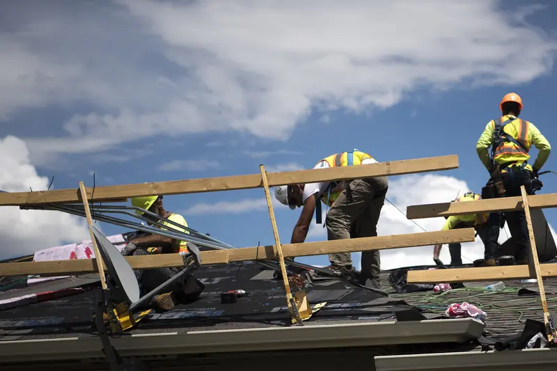 Roofing crew wearing hard hats and fall-protection harnesses installing new shingles on a house roof